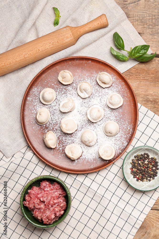 Plate with uncooked dumplings and ingredients on wooden background