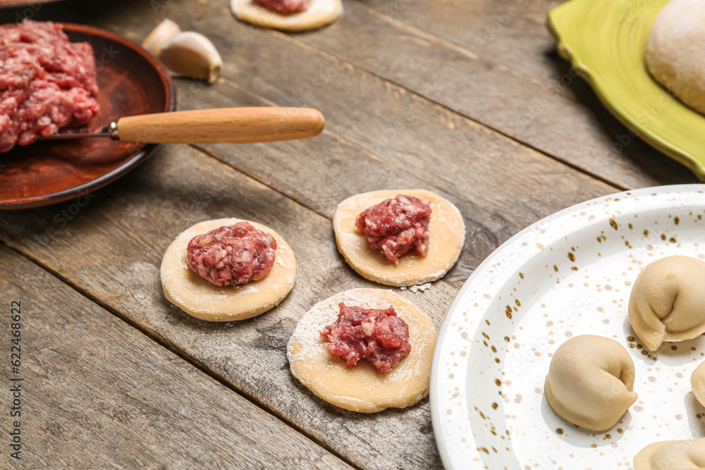 Raw dough with minced meat for preparing dumplings on wooden background