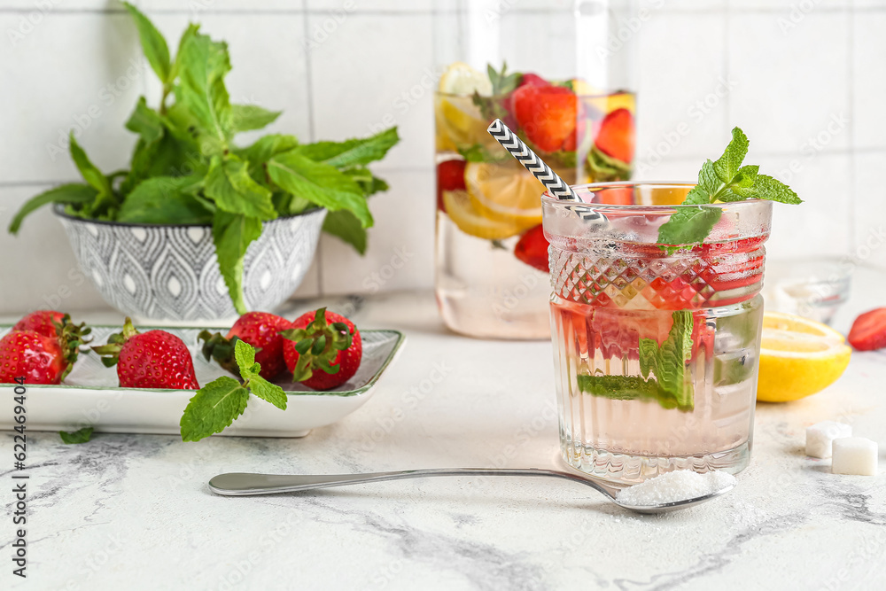 Glass and jug of fresh lemonade with strawberry on white table