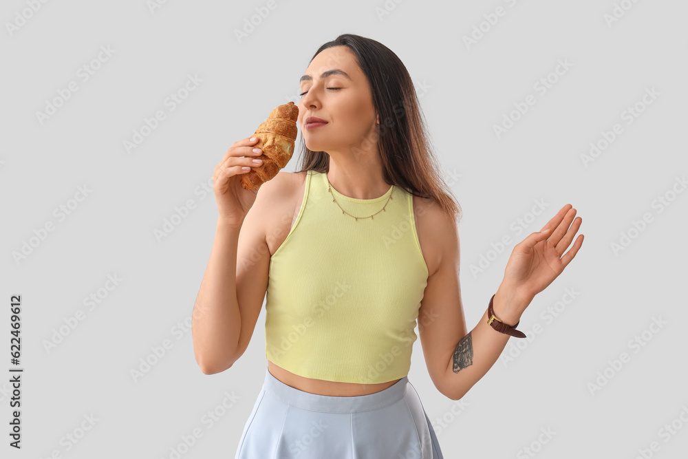 Young woman with tasty croissant on light background