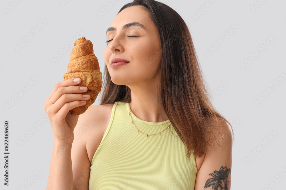 Young woman with tasty croissant on light background, closeup