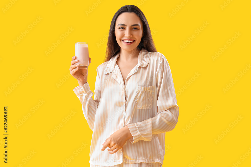 Young woman in pajamas with tasty yoghurt on yellow background