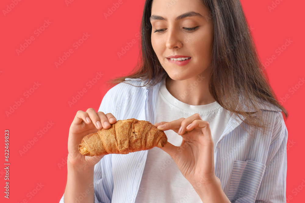 Young woman with tasty croissant on red background, closeup