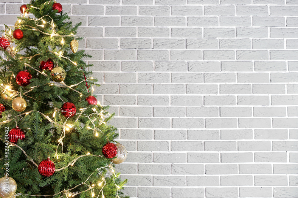 Christmas tree with glowing lights, red and golden balls near grey brick wall