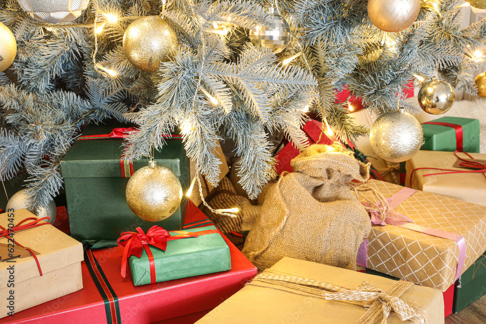 Different gift boxes under Christmas tree with glowing lights and golden balls