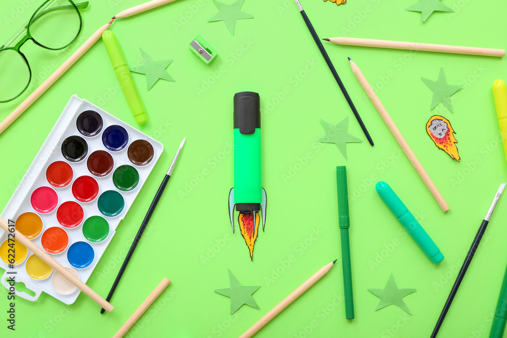 Creative composition with paper rocket, eyeglasses and different stationery on green background