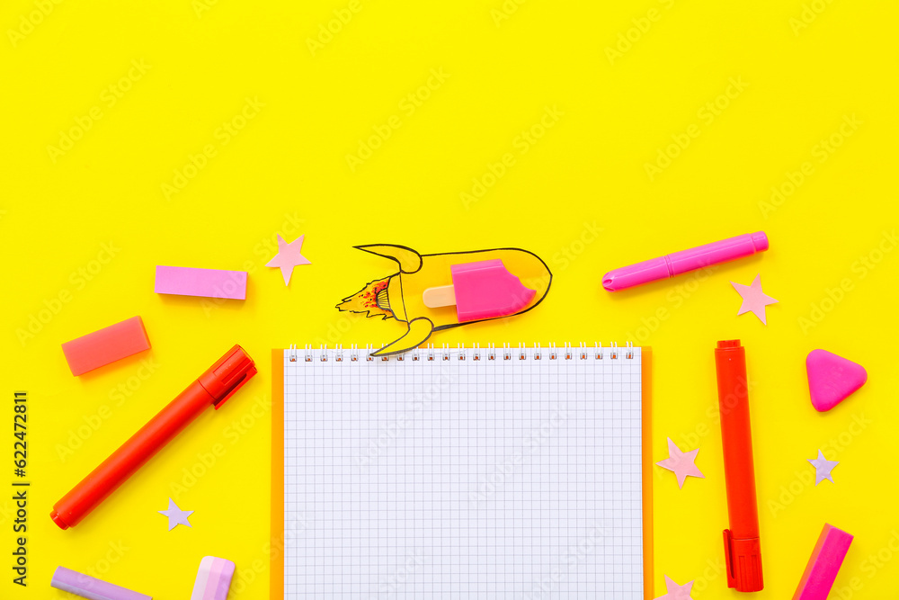 Creative composition with blank notebook, paper rocket and different stationery on yellow background