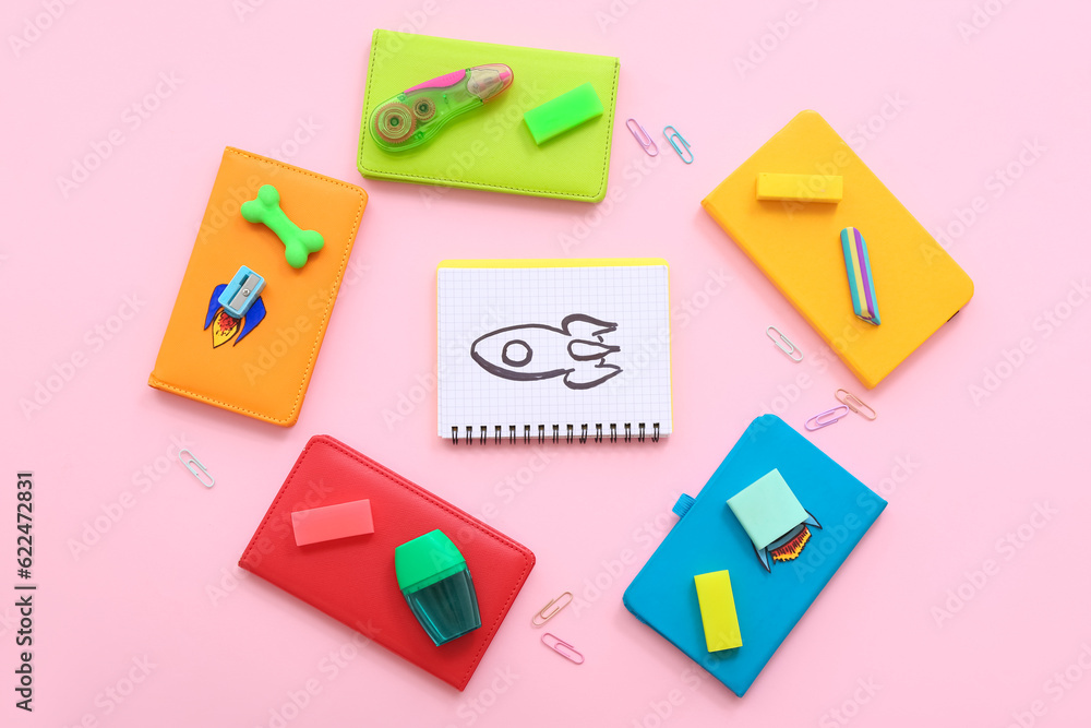 Creative composition with drawn, paper rockets and different stationery on pink background