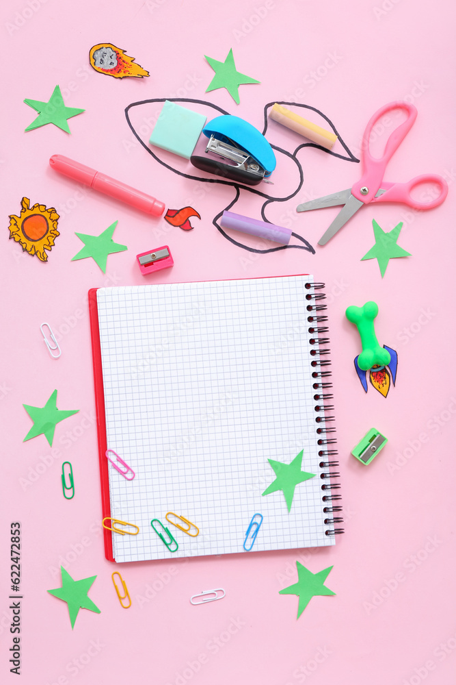 Creative composition with blank notebook, drawn rocket and different stationery on pink background