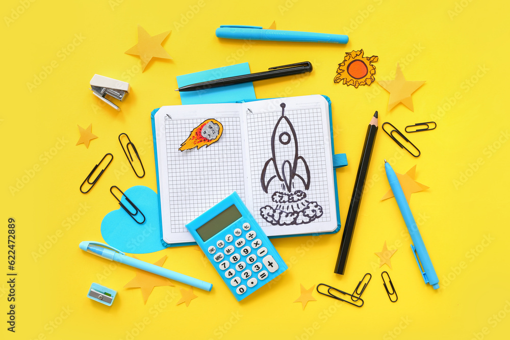 Notebook with drawn rocket, calculator and different stationery on yellow background