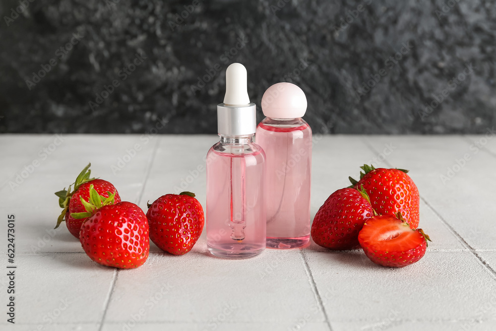 Bottles with cosmetic oil and strawberries on white tile table