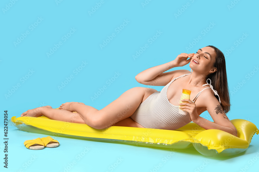 Young woman with sunscreen cream and inflatable mattress on blue background