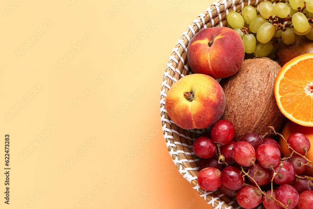 Wicker bowl with different fresh fruits on orange background