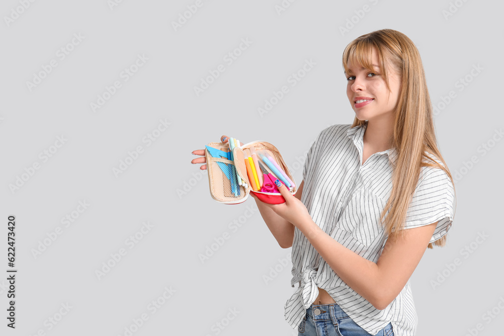 Female student with pencil case on light background