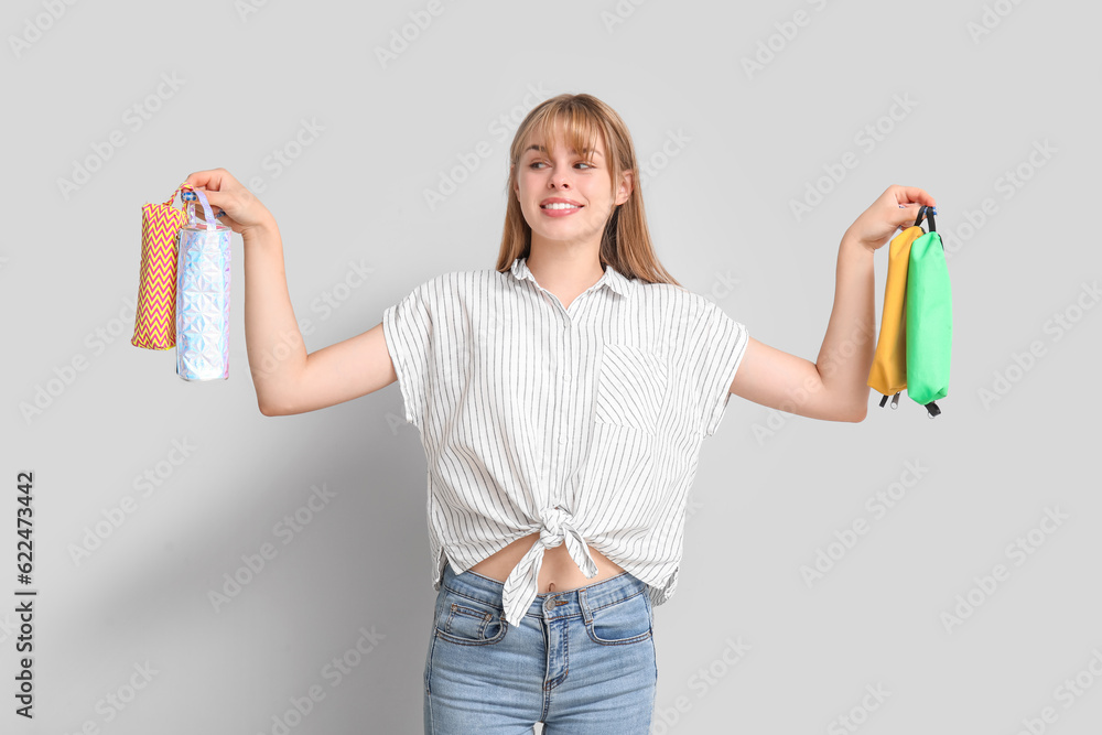 Female student with pencil cases on light background