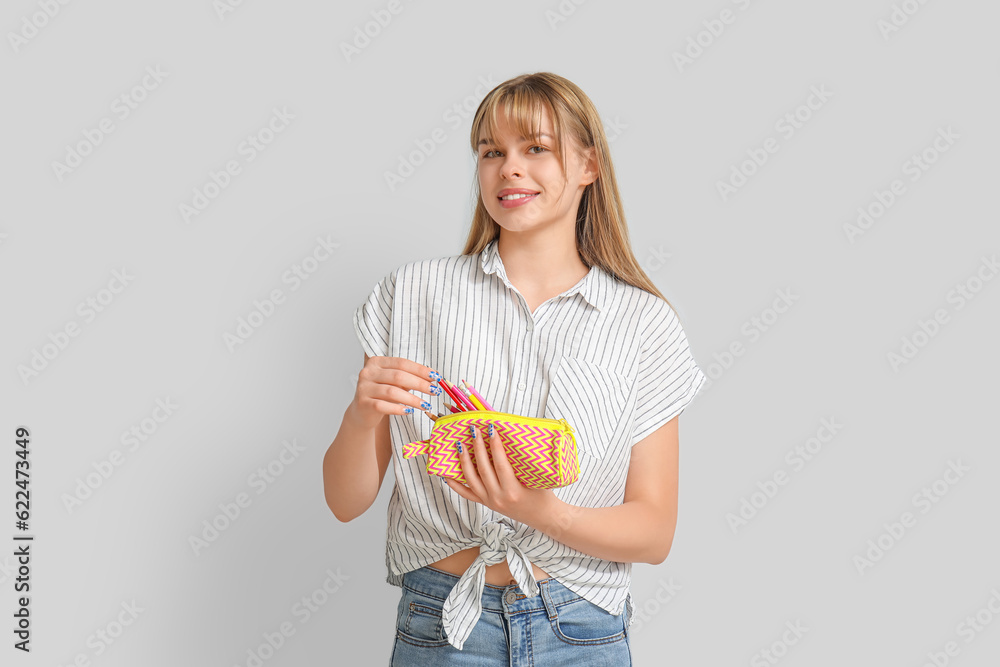 Female student with pencil case on light background