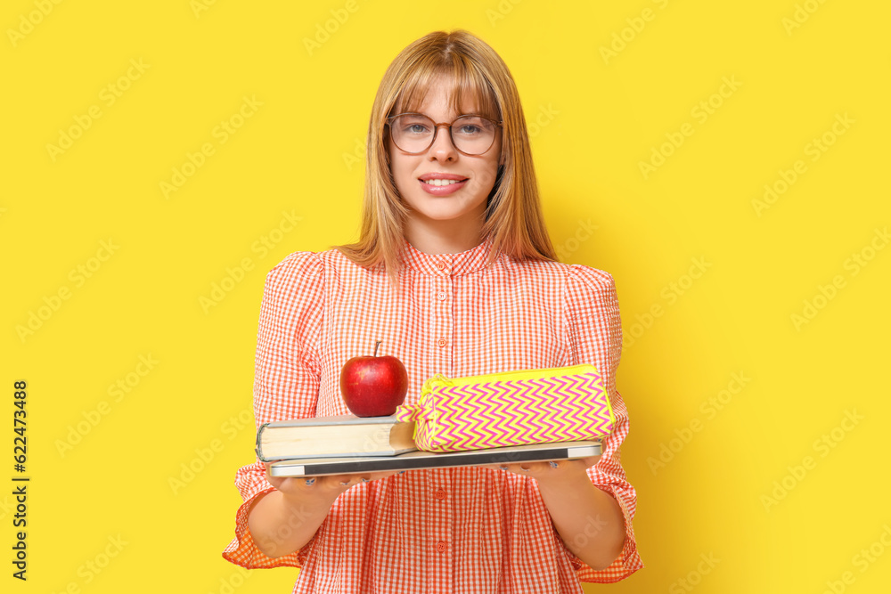 Female student with pencil case, apple, book and laptop on yellow background