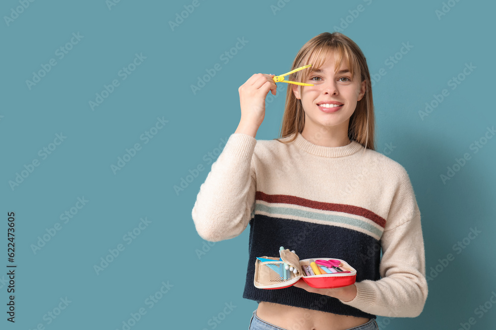 Female student with pencil case and pair of scissors on blue background