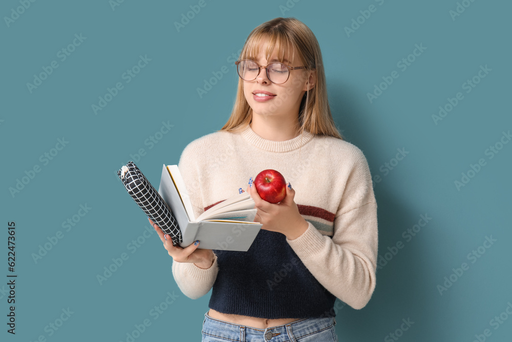 Female student with pencil case, book and apple on blue background