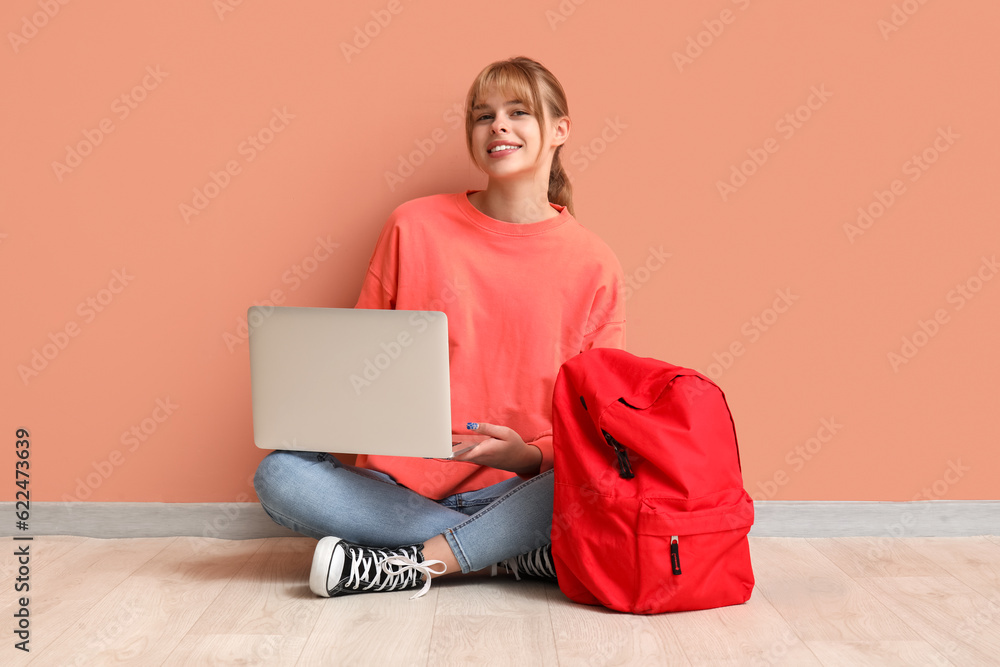 Female student with laptop and backpack sitting near color wall