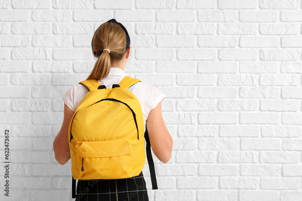 Female student with backpack on white brick background, back view