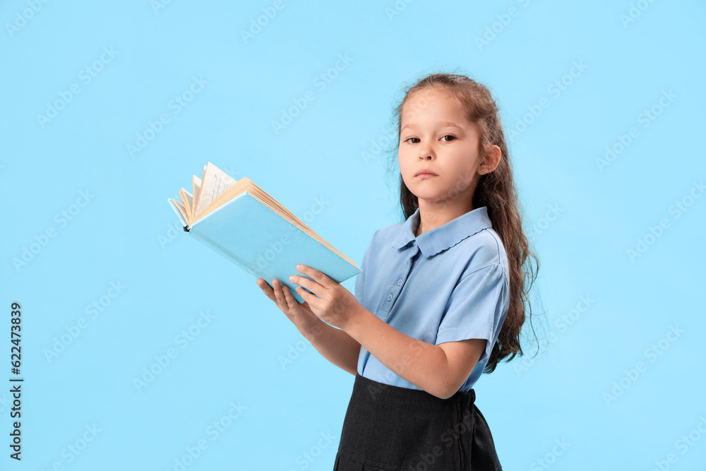 Little schoolgirl with book on light blue background