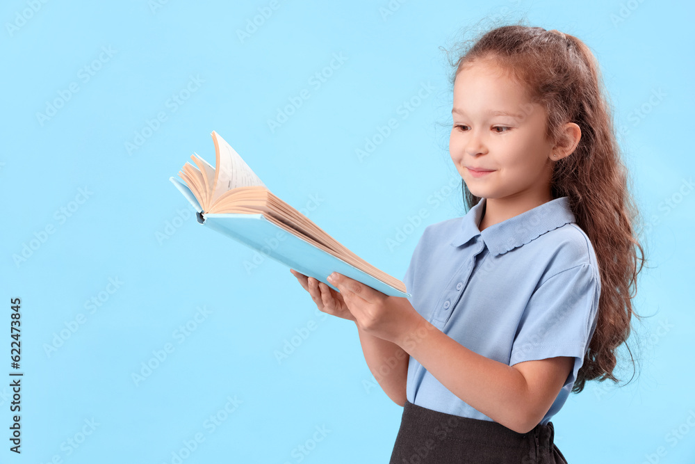 Little schoolgirl with book on light blue background