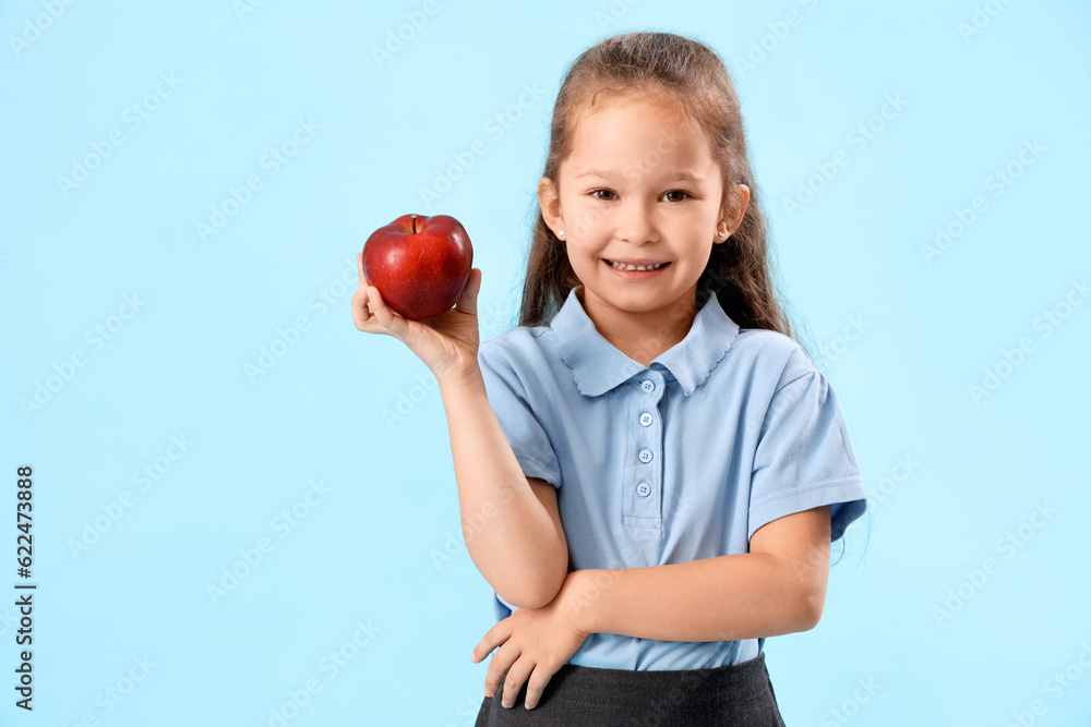 Little schoolgirl with apple on light blue background