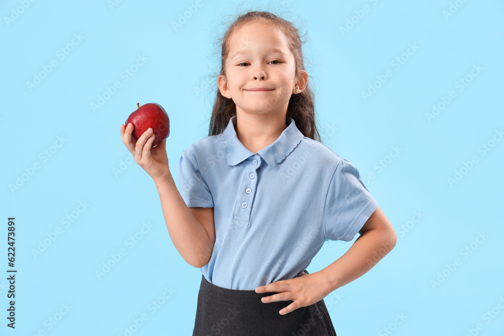 Little schoolgirl with apple on light blue background