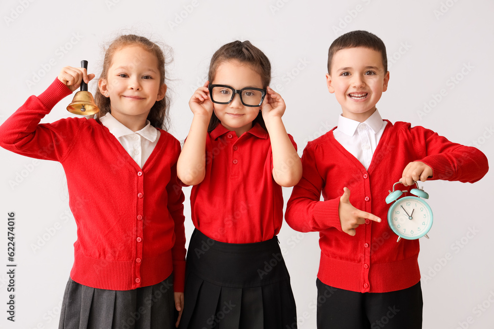 Little schoolchildren with bell and alarm clock on grey background