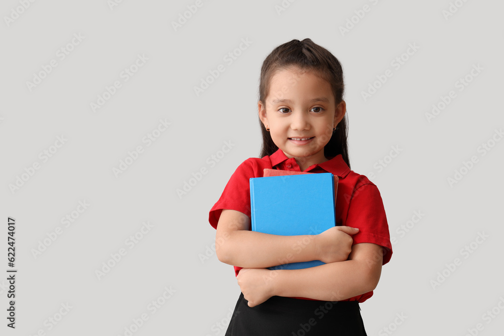 Little schoolgirl with book on grey background