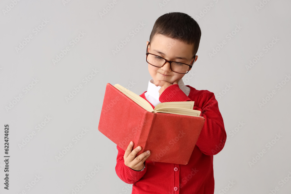 Little schoolboy with book on grey background