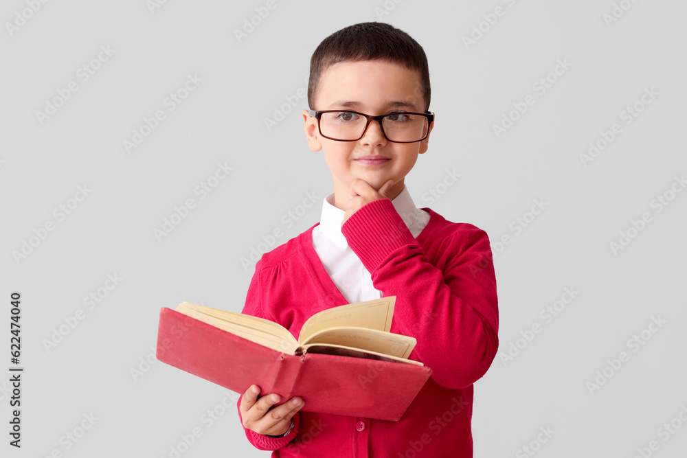 Little schoolboy with book on grey background