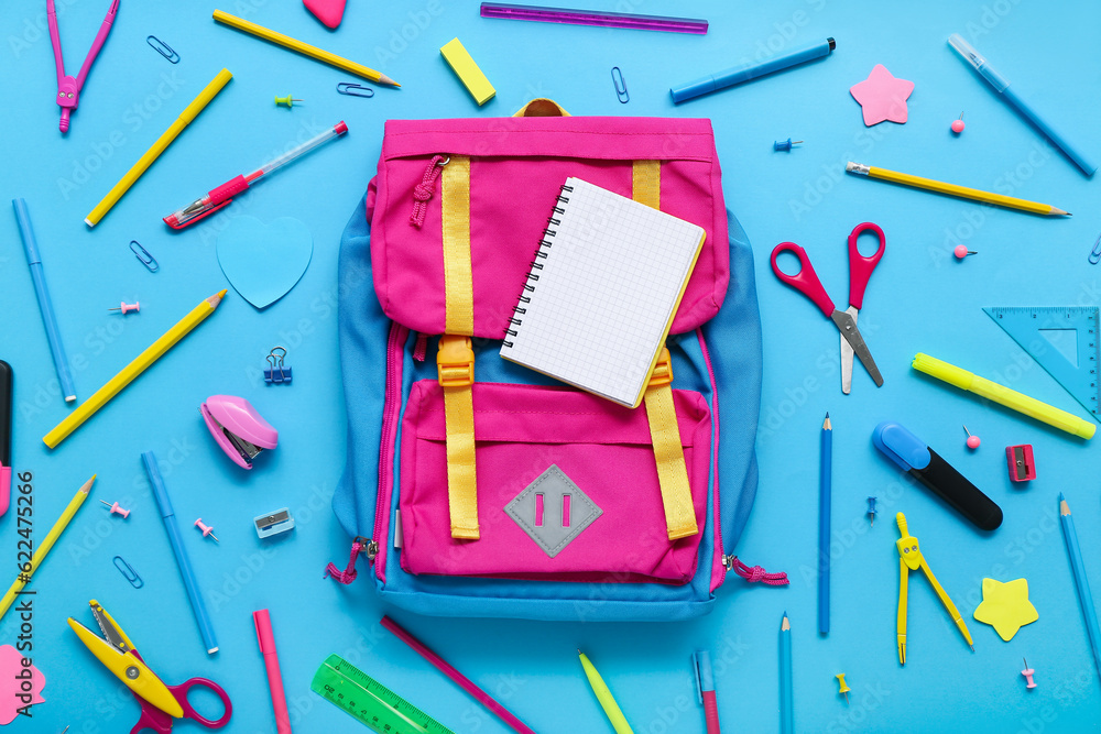 Backpack with blank notebook and different stationery on blue background