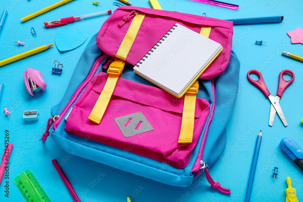 Backpack with blank notebook and different stationery on blue background