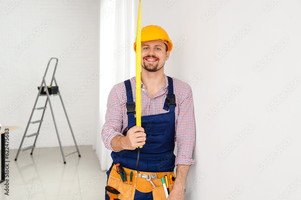 Male builder with tape measure in room