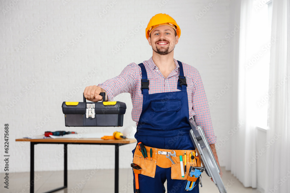 Male builder with tool bag and stepladder in room