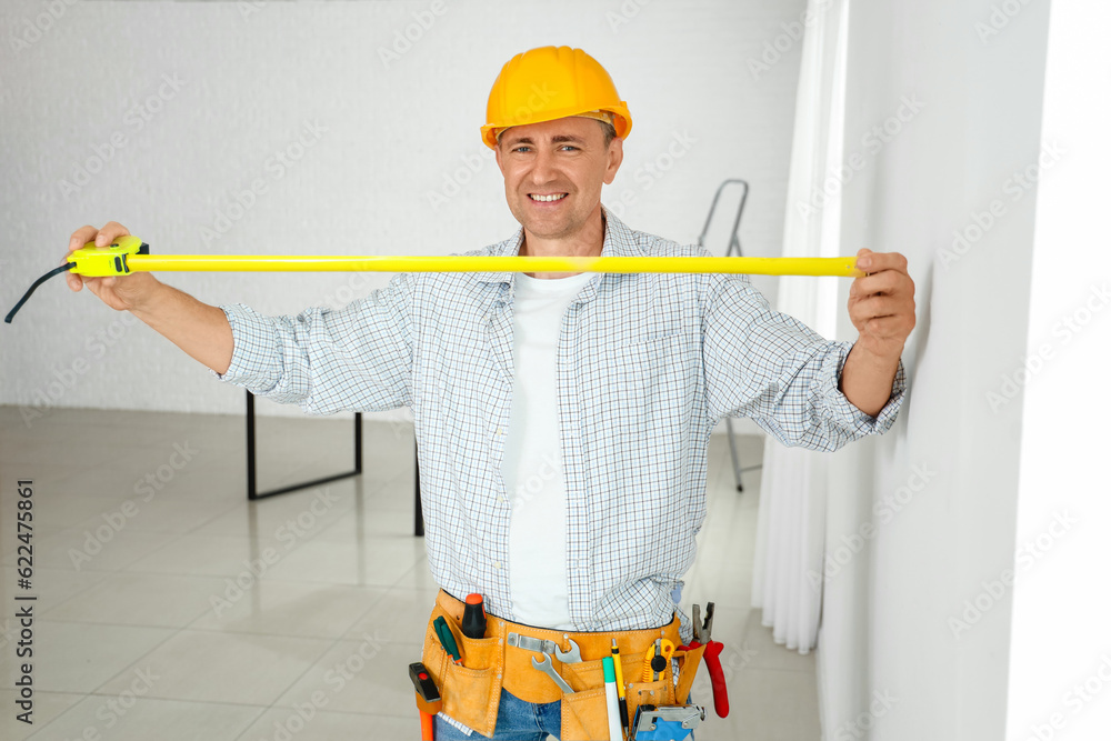 Mature builder working with tape measure in room