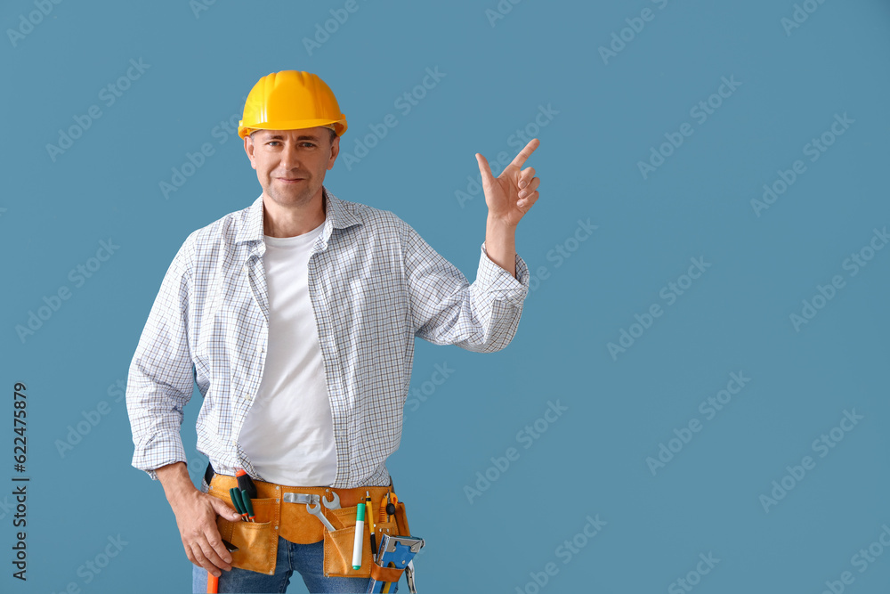 Mature builder with tool belt pointing at something on blue background