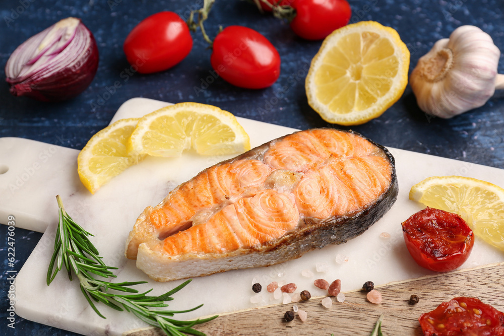 Board with tasty grilled salmon steak on blue background