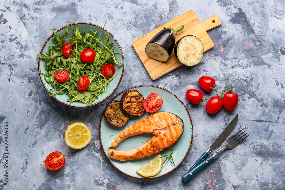 Plate with tasty grilled salmon steak and vegetables on blue background