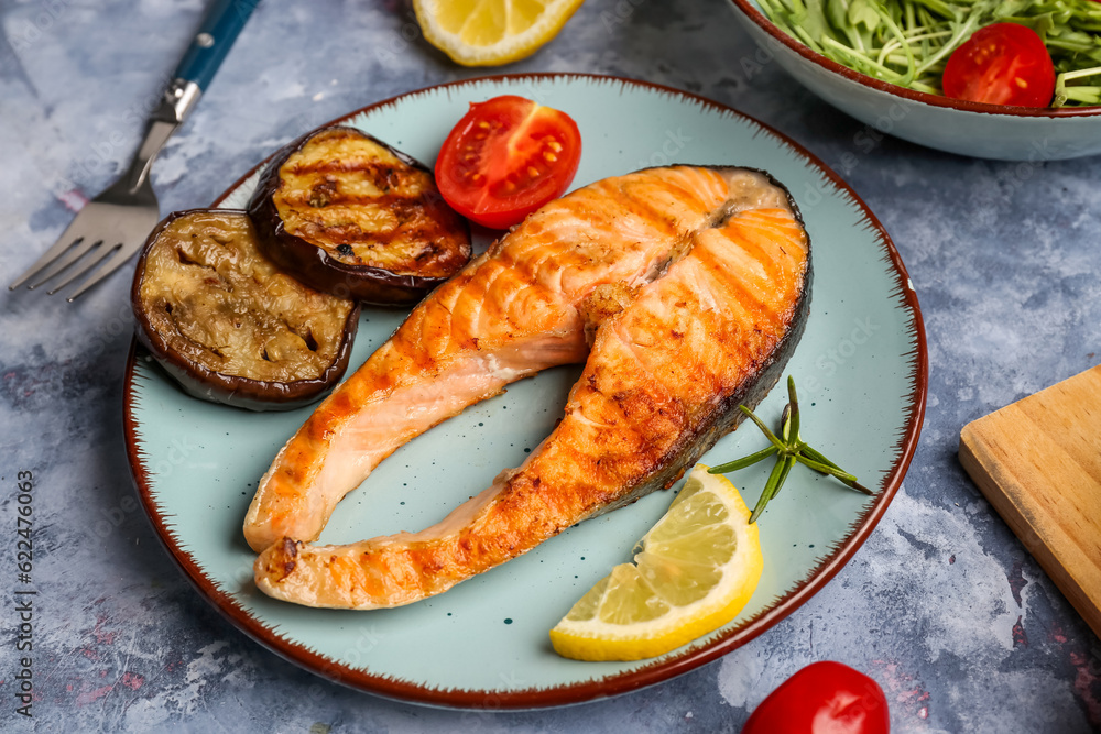 Plate with tasty grilled salmon steak and vegetables on blue background