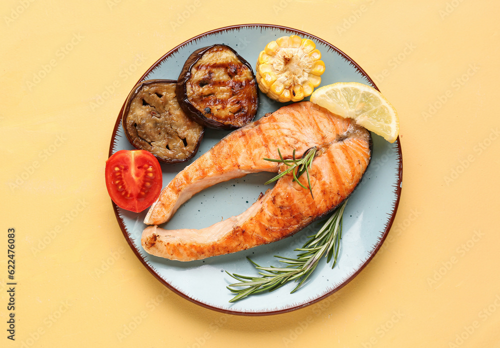 Plate with tasty grilled salmon steak and vegetables on yellow background