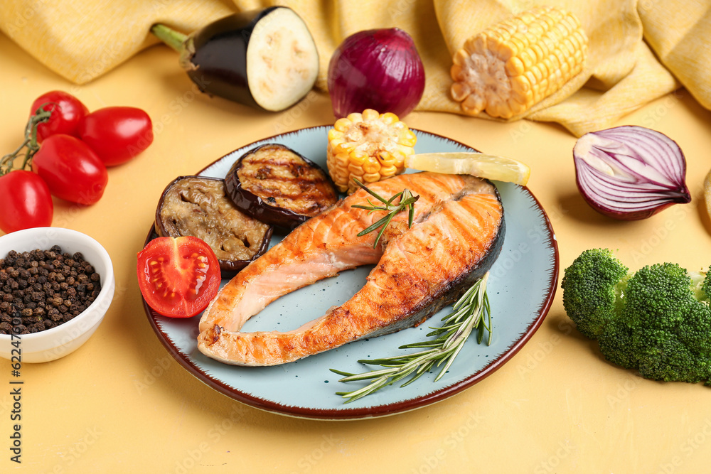 Plate with tasty grilled salmon steak and vegetables on yellow background