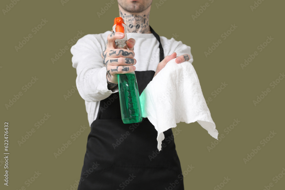 Young tattooed man with bottle of detergent and rag on green background, closeup