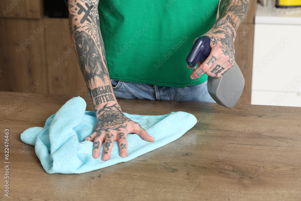 Young tattooed man cleaning dining table in kitchen, closeup