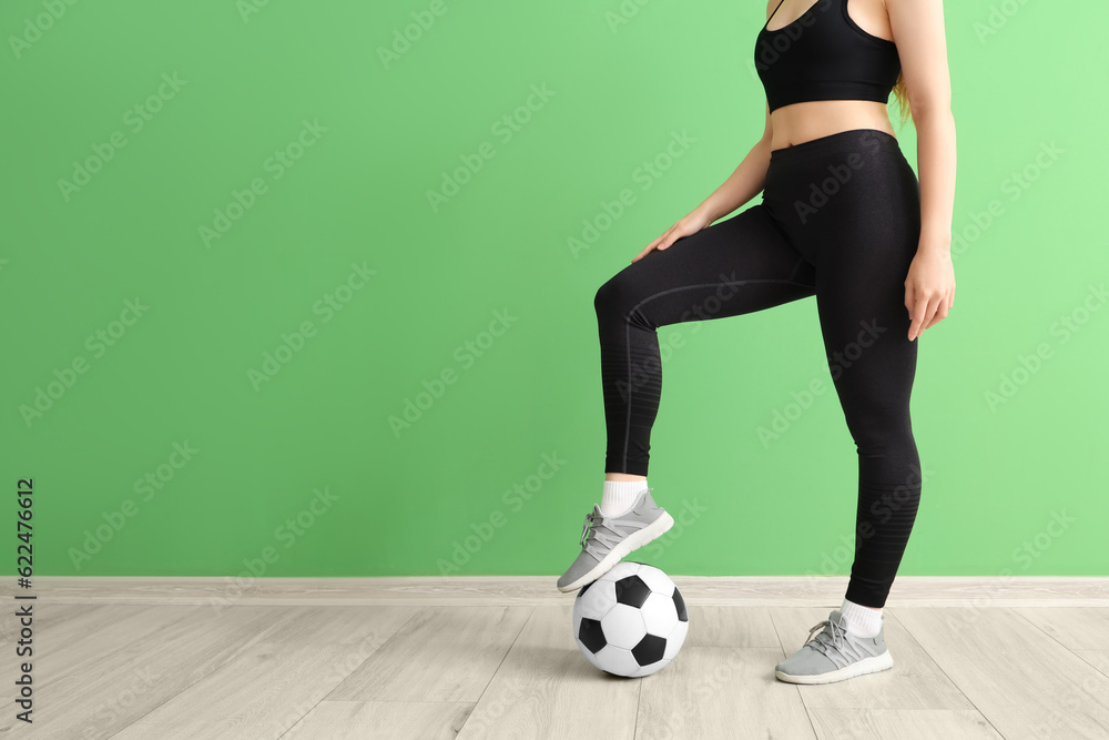 Young woman in sportswear and with soccer ball near green wall