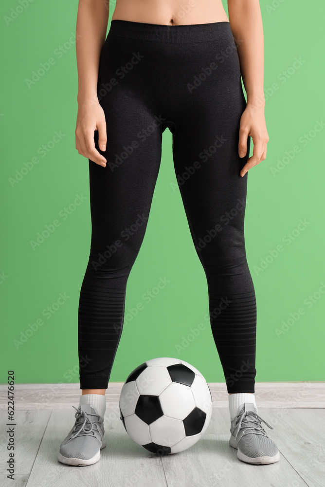 Young woman in sportswear and with soccer ball near green wall