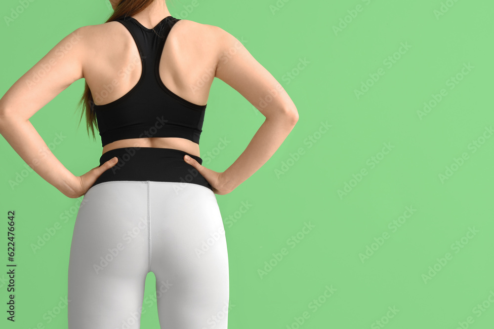 Young woman in sportswear on green background, back view