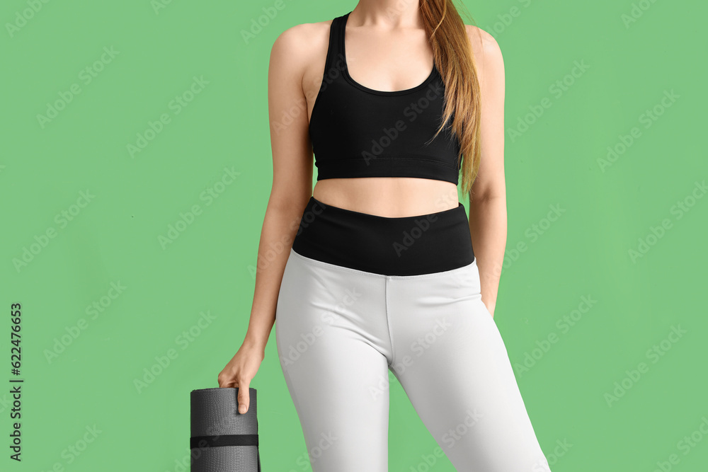 Young woman in sportswear and with yoga mat on green background